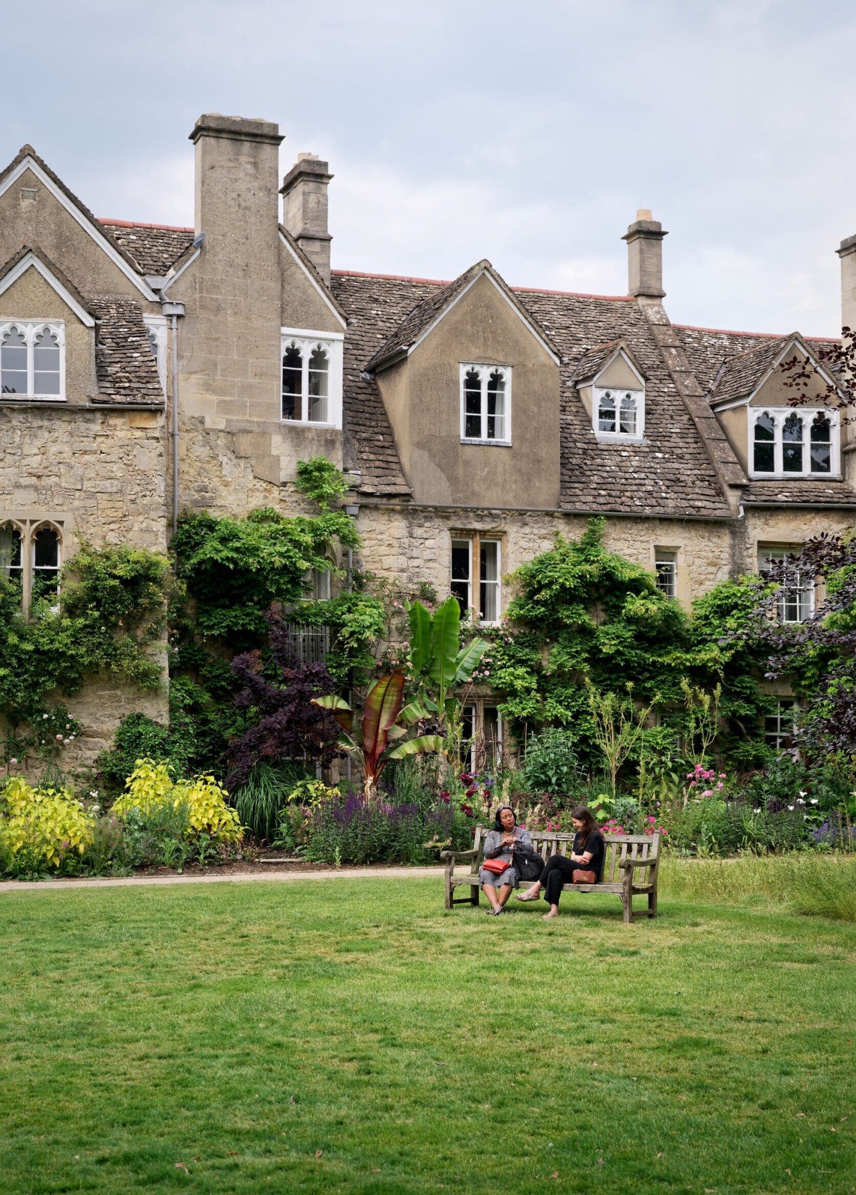 Two people sat on a bench in front of the cottages and long border