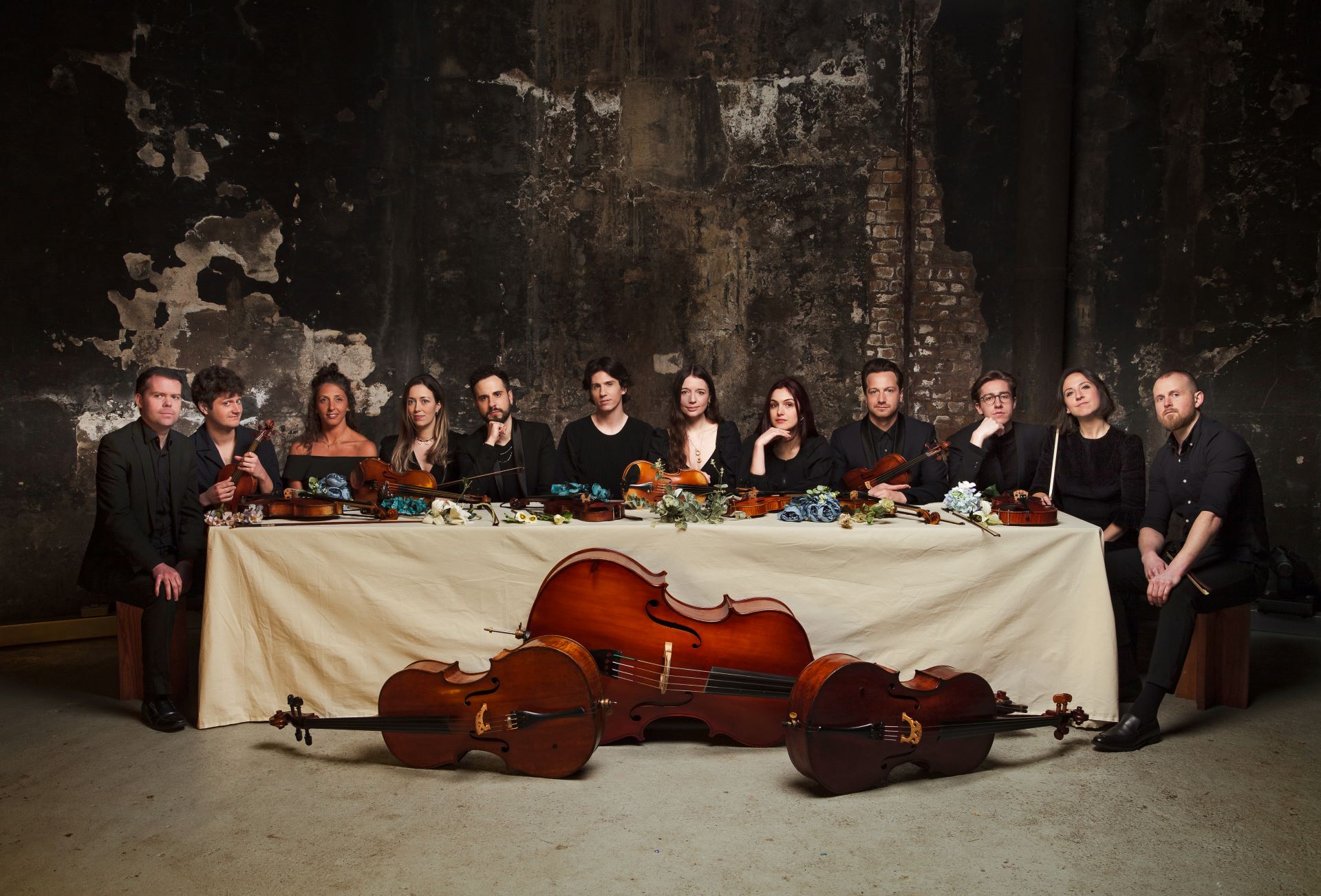 12 Ensemble sat at a long table covered with flowers and string instruments