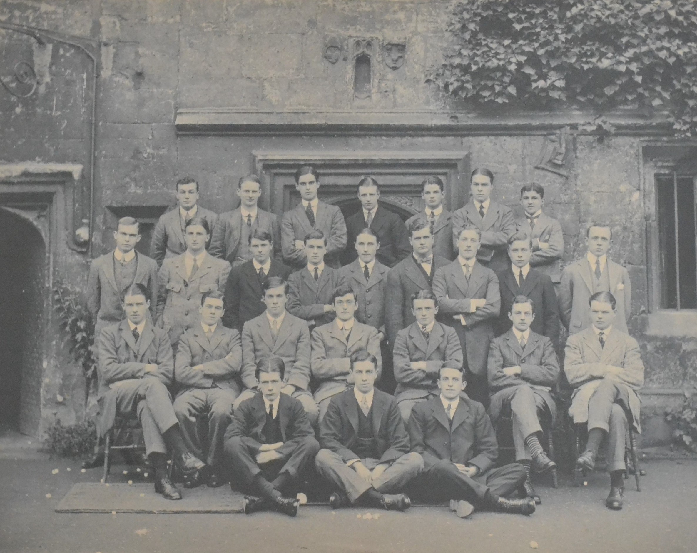 Black and white photograph of 26 young men, taken in front of the medieval cottages.