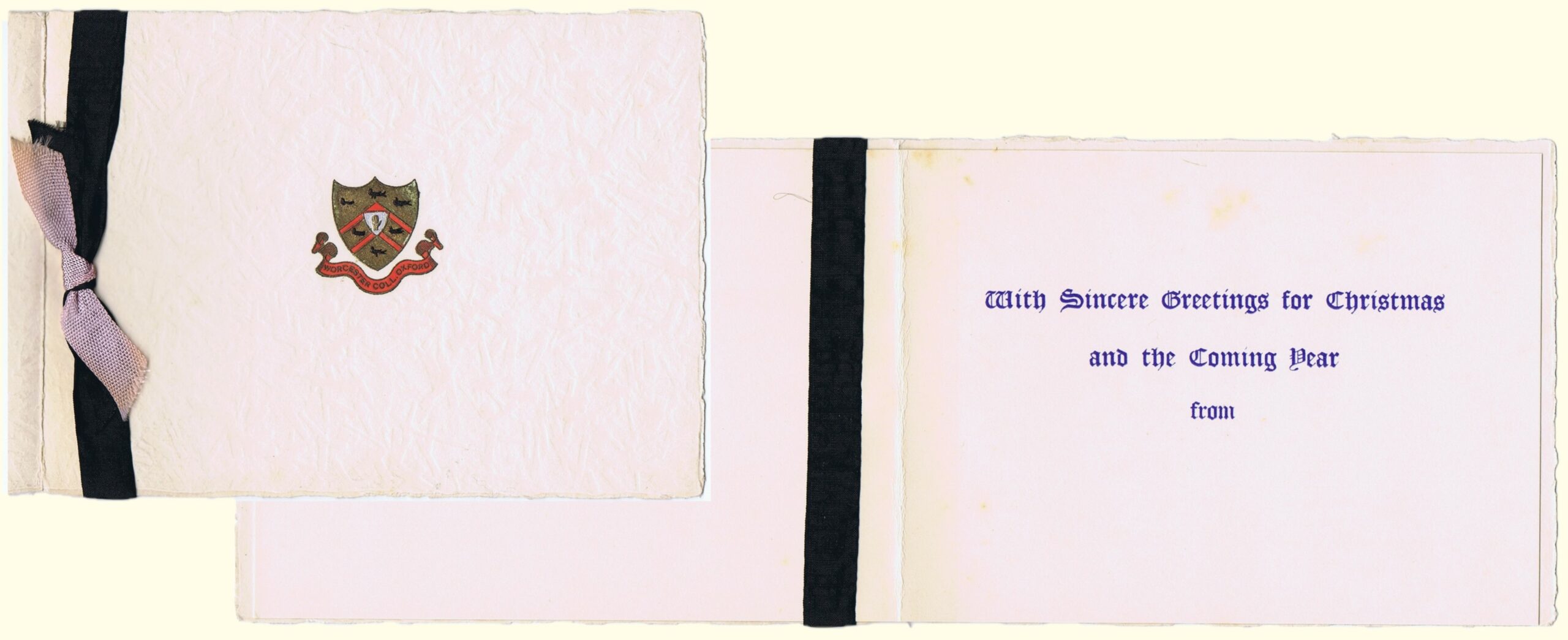 Image of a plain white card with the college crest in red and gold on the front, with a pink and black ribbon down the side. Inside the card are Christmas wishes in blue gothic type.