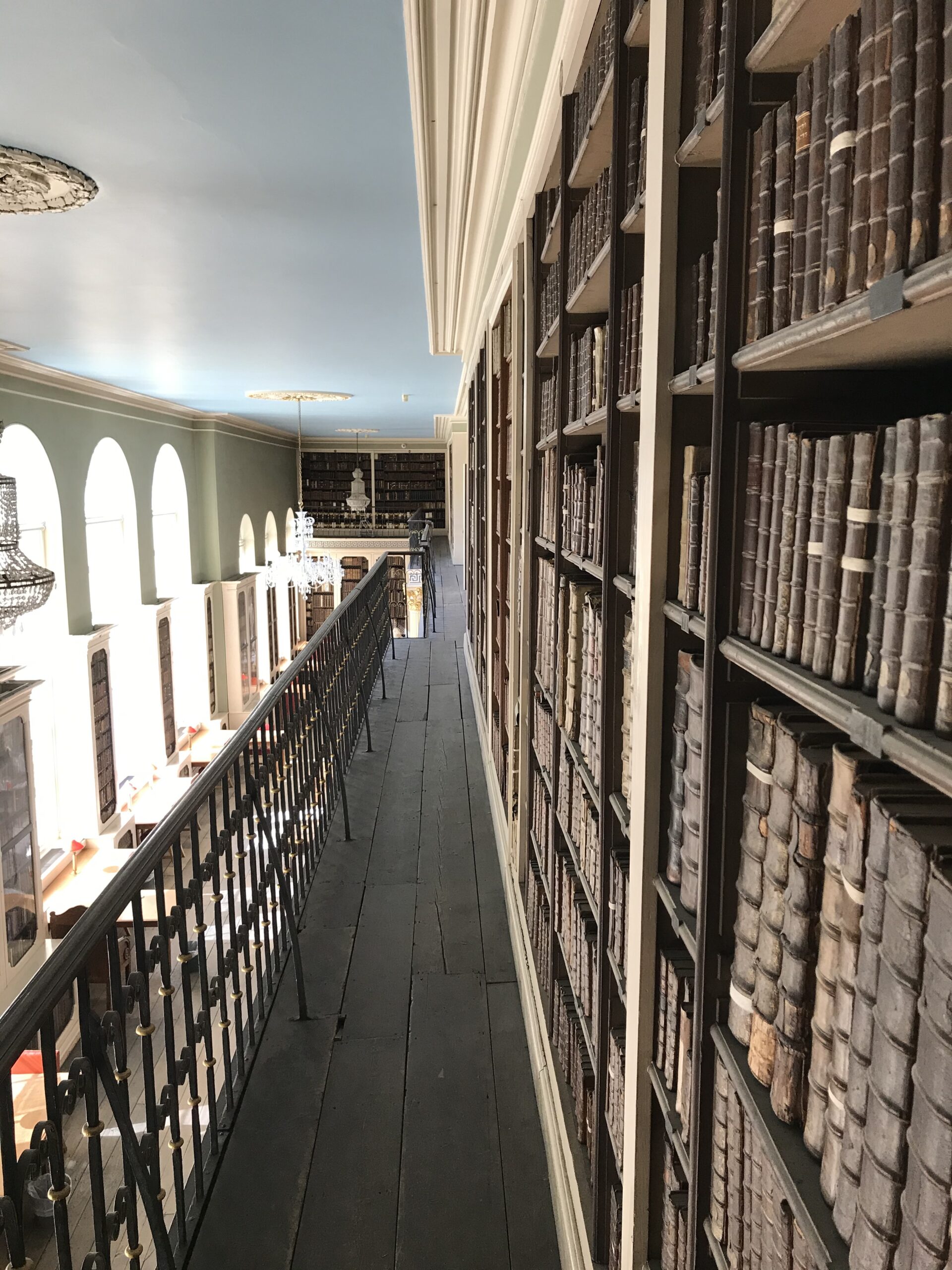 A view from the Library gallery - with bookshelves running into the distance on the right and three large windows to the left.