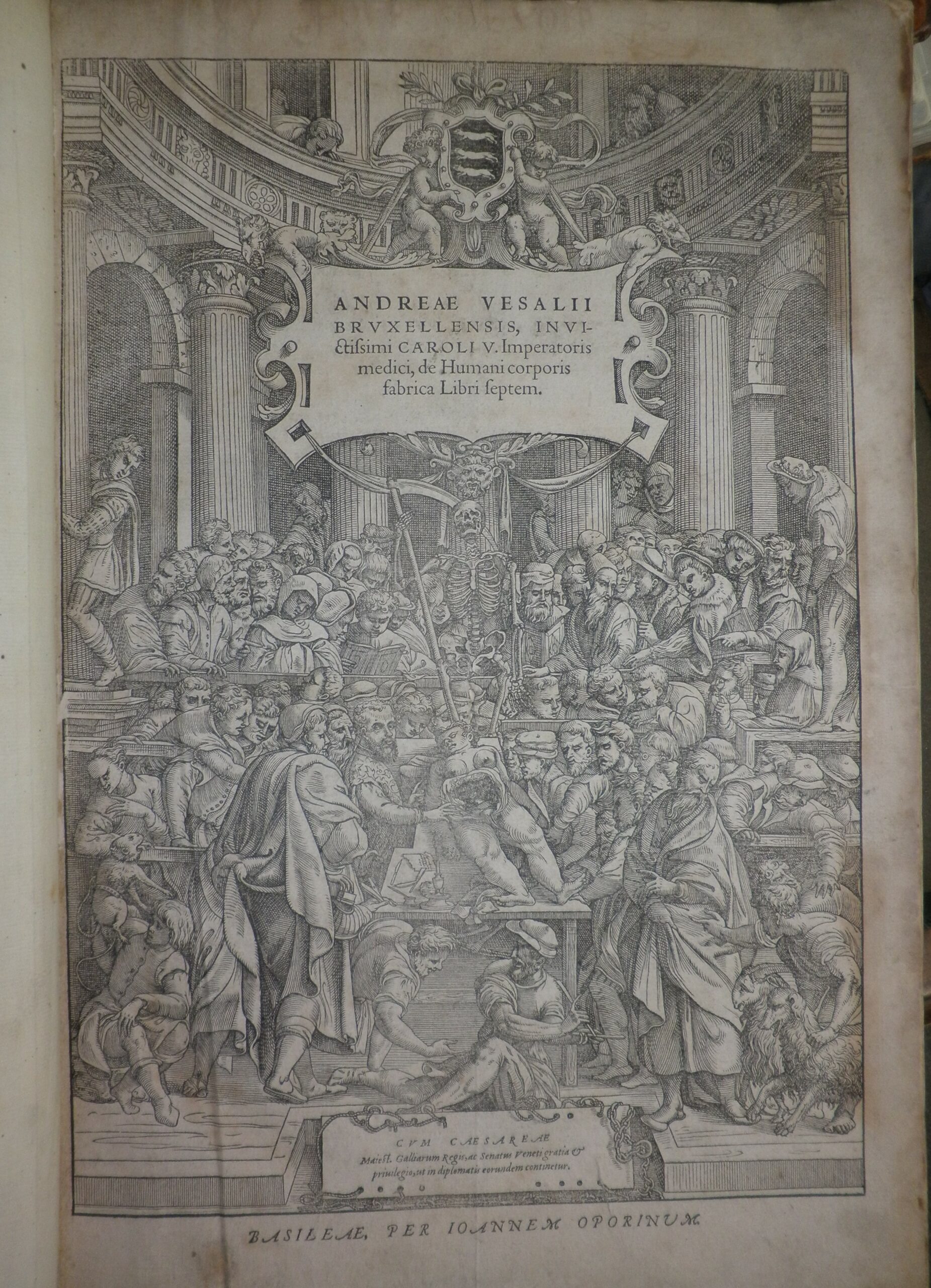 Title page of Vesalius' De corporis humani fabrica. The background is a full page copperplate image of a crowded dissection theatre. A dissection is taking place in the centre of the image.