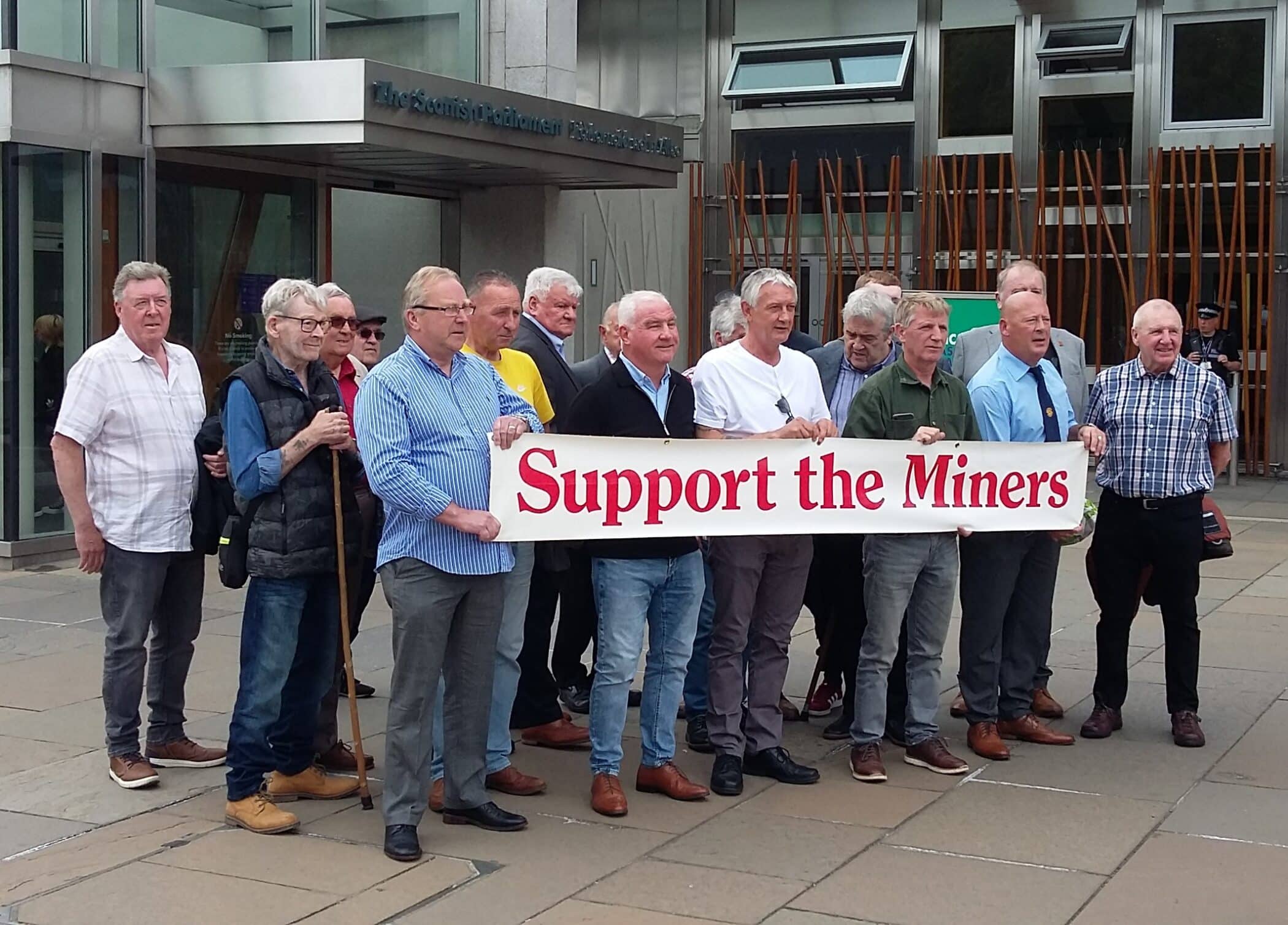 Group of ex-miners holding a support the miners sign outside the Scottish Parliament