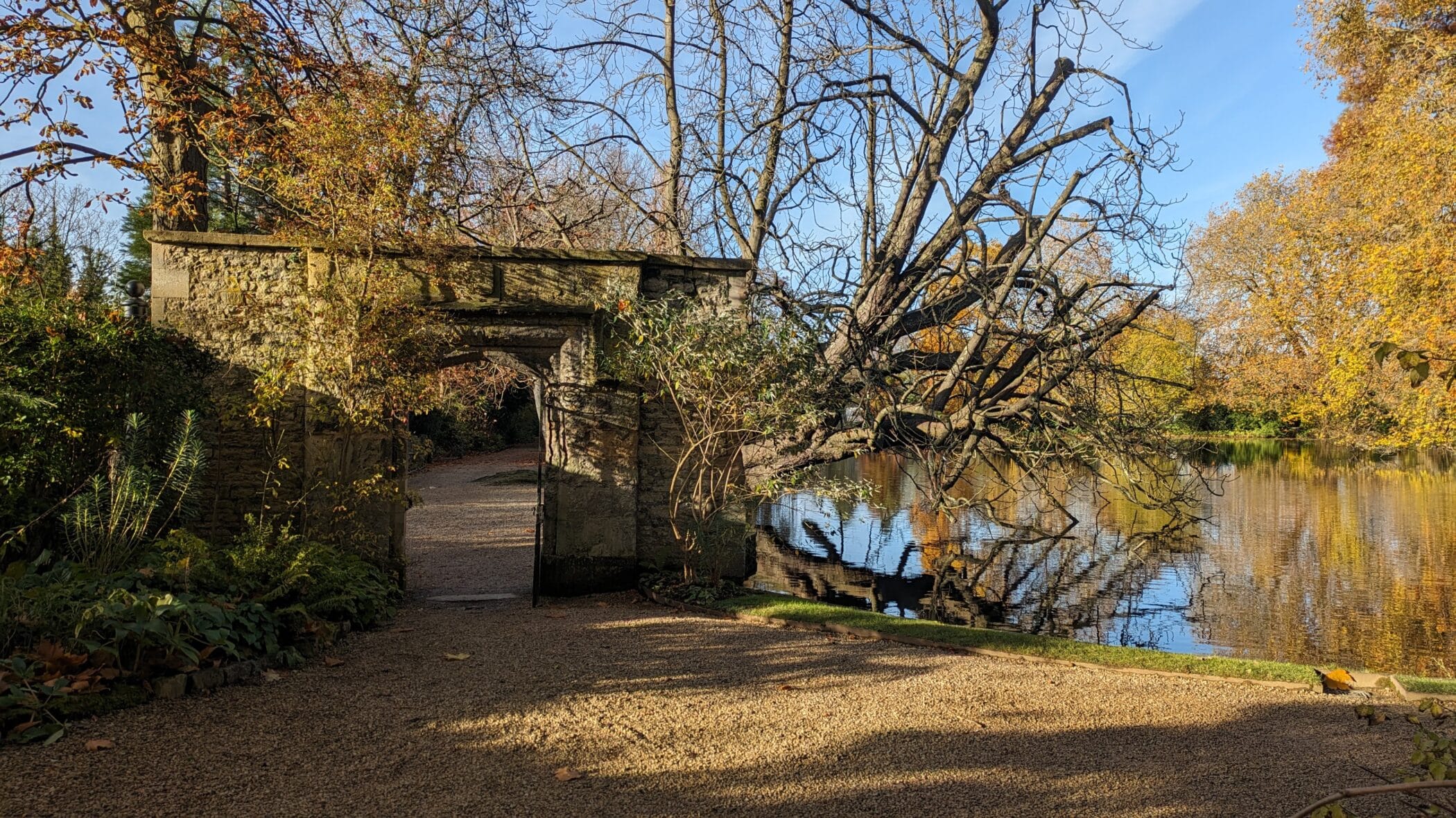Stone archway beside lake with autumnal trees