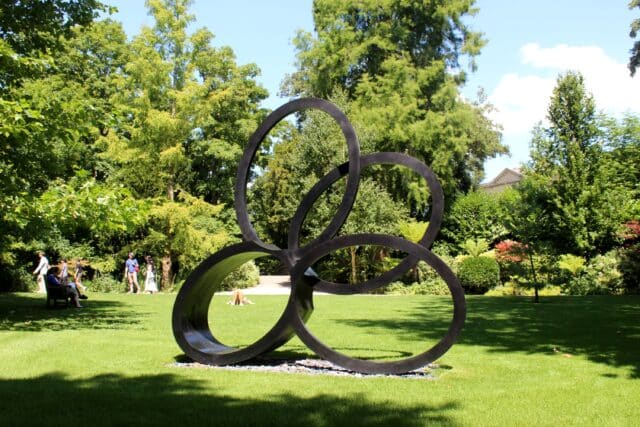 Contemporary bronze sculpture of intersecting ovoids in natural setting of grass and trees