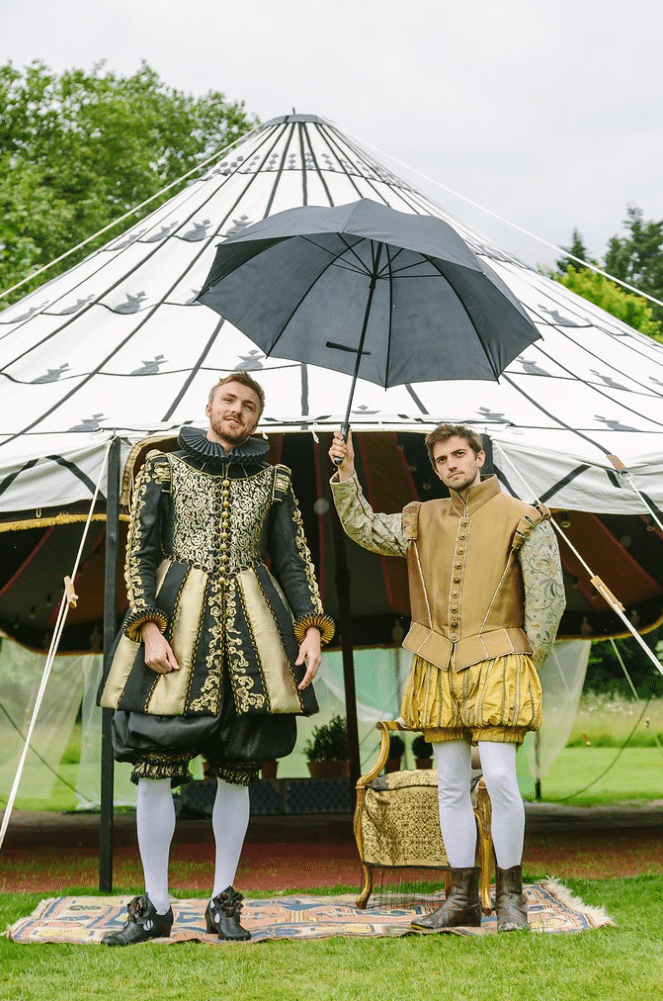 Two actors in period dress holding an umbrella